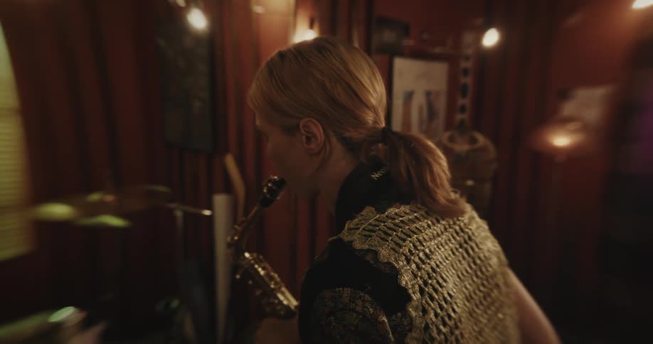 A woman is standing inside a room playing a saxophone