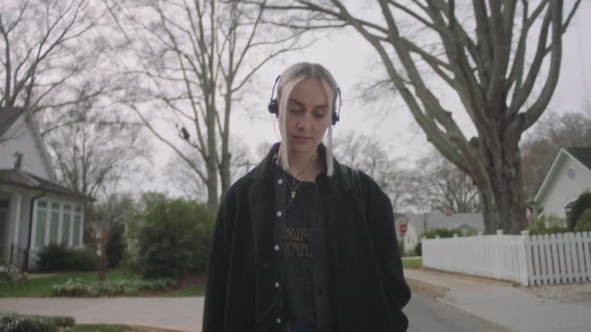 Woman walking in the tail of a residential neighborhood with headphones on a cloudy day