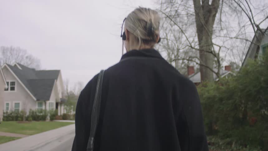 Back of a lady walking on the sidewalk in a suburb area during the day