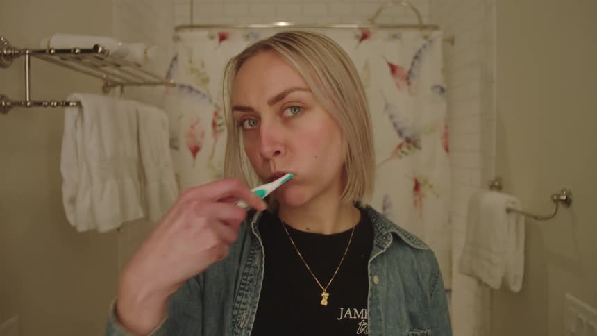 Portrait of a young woman brushing her teeth in the bathroom