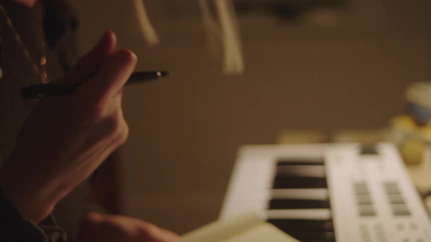 A female gesticulating while holding a pen and book indoor