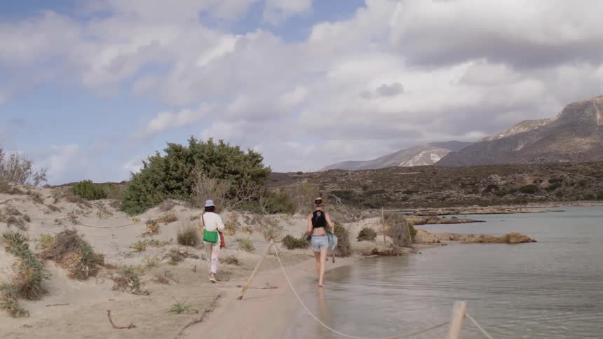 Two people walking along the shore of a lake with mountains in the horizon