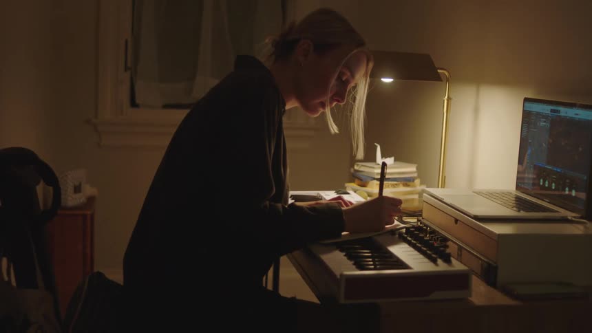 Woman sits at desk and composes in notebook over keyboard