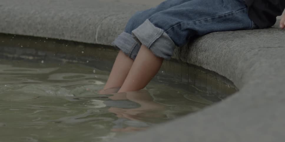 A person wearing rolled up jeans steps into a shallow concrete pool