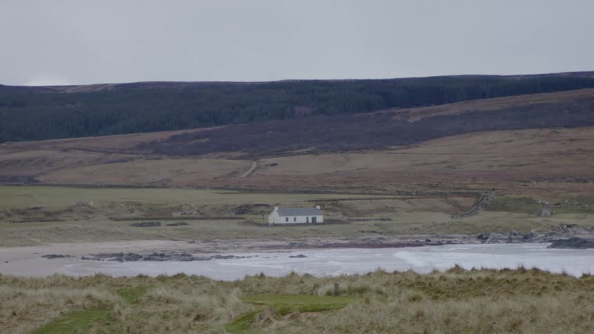 Panorama of a sea amidst grassland with a farmhouse on the horizon