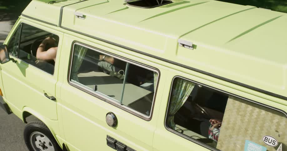 A man driving a lemon van with some bicycle strap to the back of the van