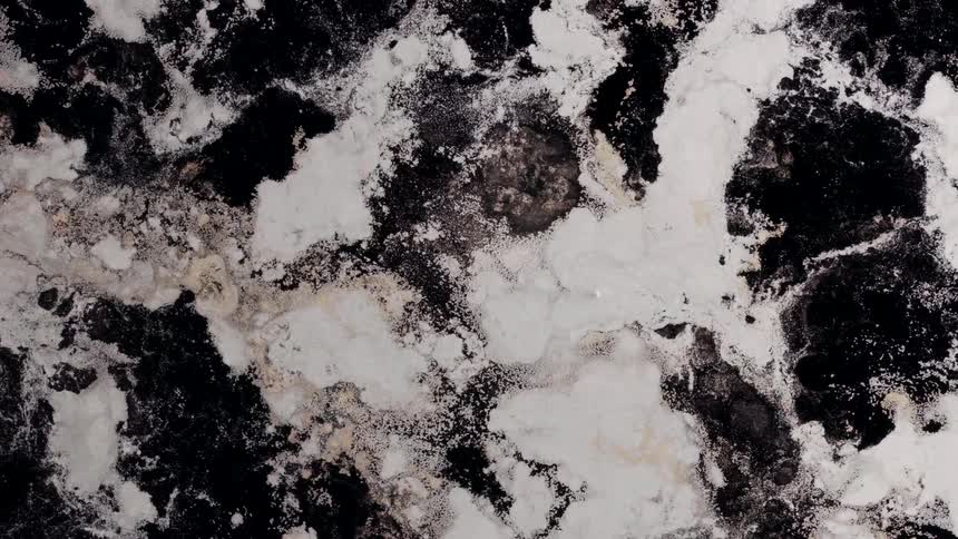 Ice breaks apart as it floats across churning black water