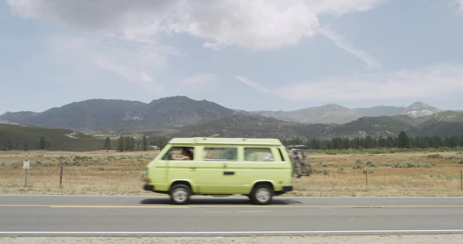 A van with bicycles on the back travels on a desert road with mountains in the distance