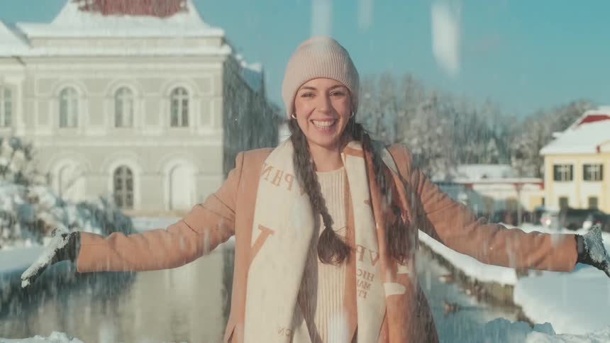 A young woman playfully throws snow into the air so that it falls on herself