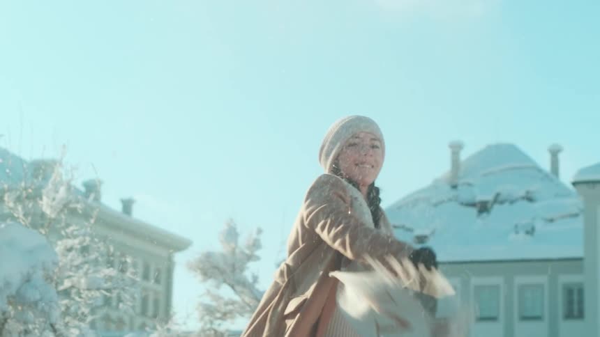 Woman wearing beanie tosses snowball outside in winter