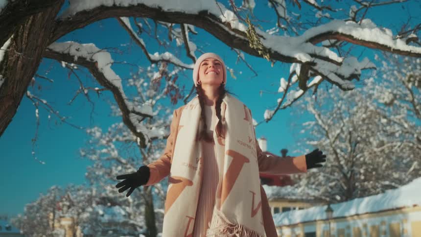Woman walking on a snowcovered city sidewalk happily reaching for a branch on a tree