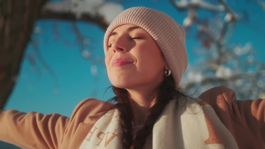 Portrait of a woman feeling joyful and opening her arms in a snowy environment with a blue sky