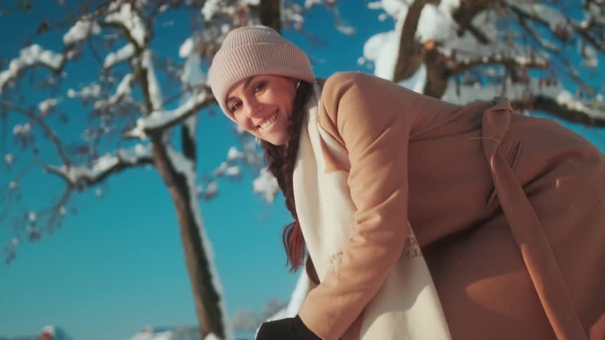 Woman in the snow picking up a snowball with her hands