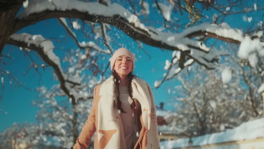 A happy woman knocking snow from a tree branch