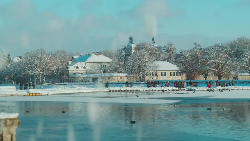 Panorama of a park with a lake and several people around in the midst of snow