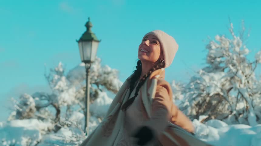 Portrait of a young woman in a coat happily twirling in a snowy environment on a day with a blue sky