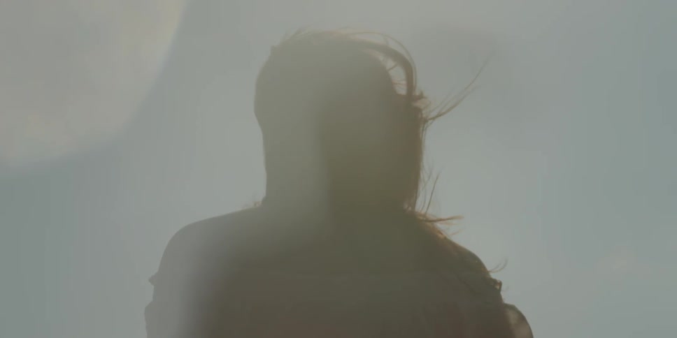 A woman stands outside on a windy and sunny day as her hair blows around