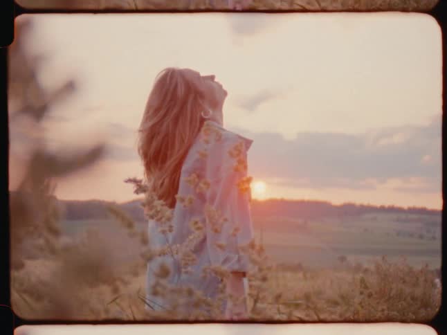 Woman in nature amidst a grassland looking up with the sunset on the horizon