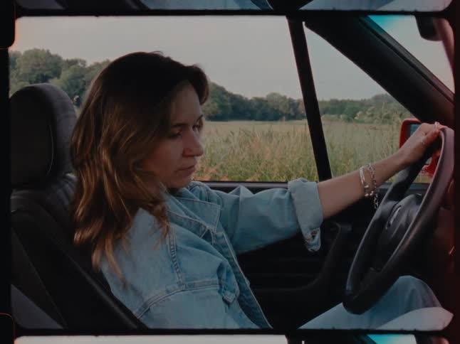 A clip of a lady sitting in a car in the middle of the forest