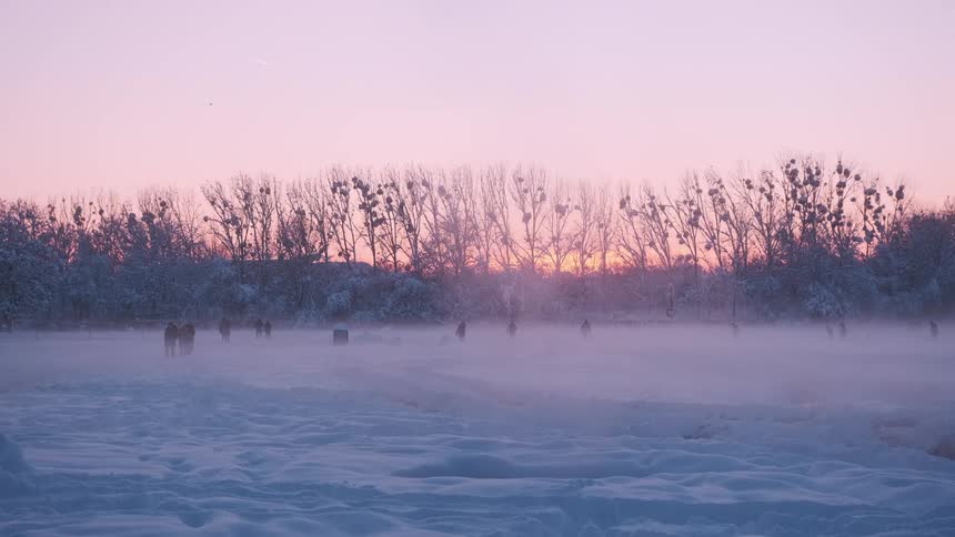People walk through snow covered park at dusk