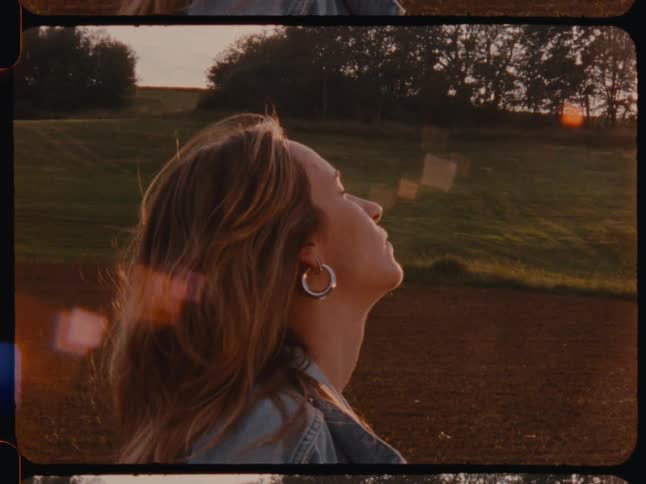 Woman in the midst of a field with her face turned sideways and eyes closed with a sunlit reflection