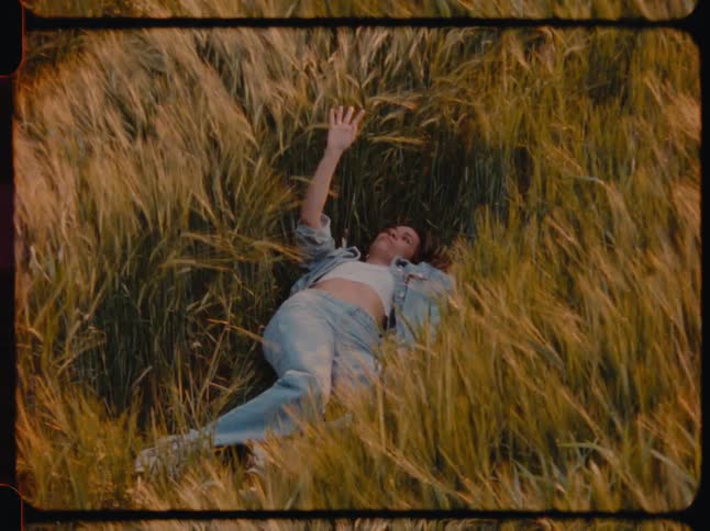 A woman lays on her back in a field of tall grass while holding up her hand
