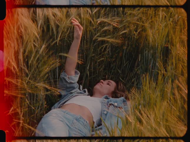 Woman wearing a denim jacket and jeans lies in a wheat field