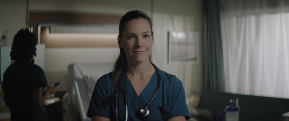 A female doctor stands still in a hospital room and smiles