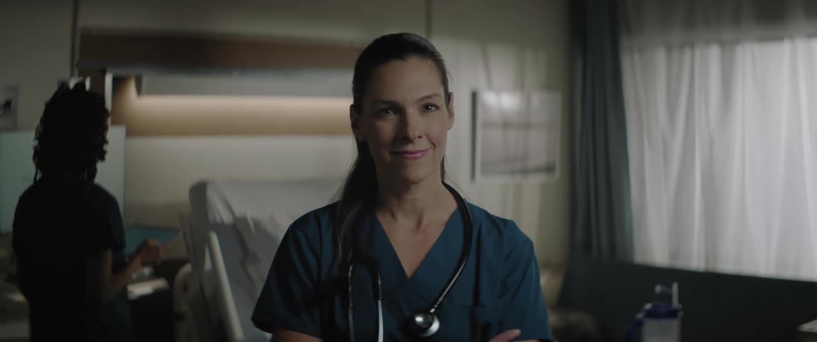 Two women wearing scrubs stand in hospital room near bed