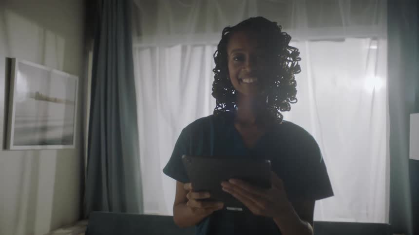 A nurse smiling while looking at a computer tablet in an hospital room at midday