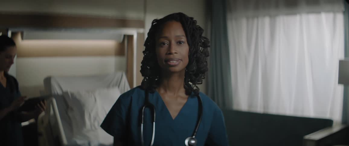 Woman wearing scrubs smiles standing near hospital bed