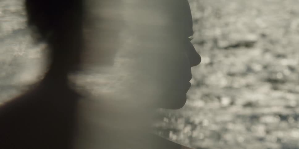 A woman stares into the glistening ocean water