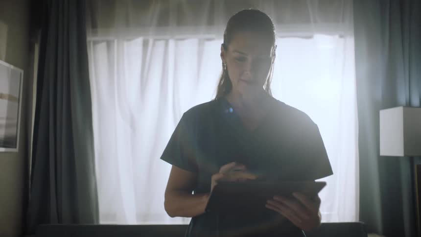 A young doctor walks next to a hospital bed while typing on an electronic tablet