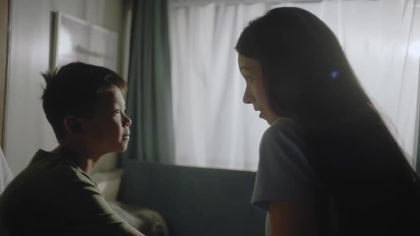 A mother and son are sitting down in a room while talking to each other