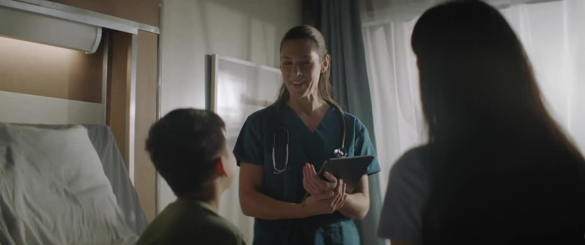 A female doctor smiles while talking to a mother and son in a hospital room