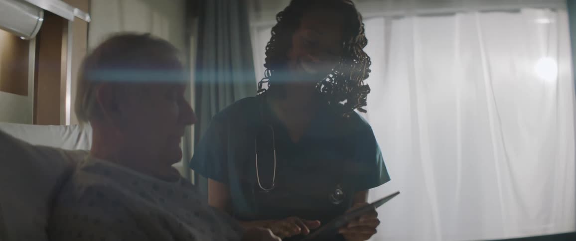 Smiling nurse showing something on a tablet to an elderly patient in bed
