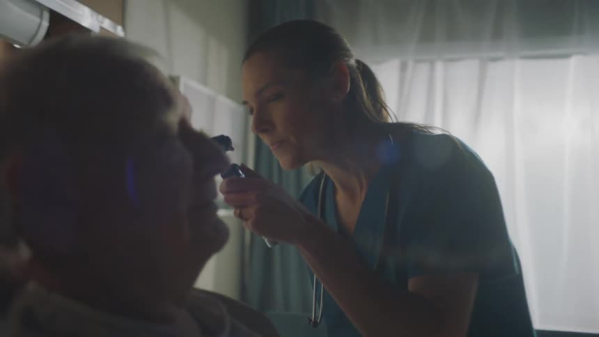 Female medical professional examines elderly male patients ear in hospital room
