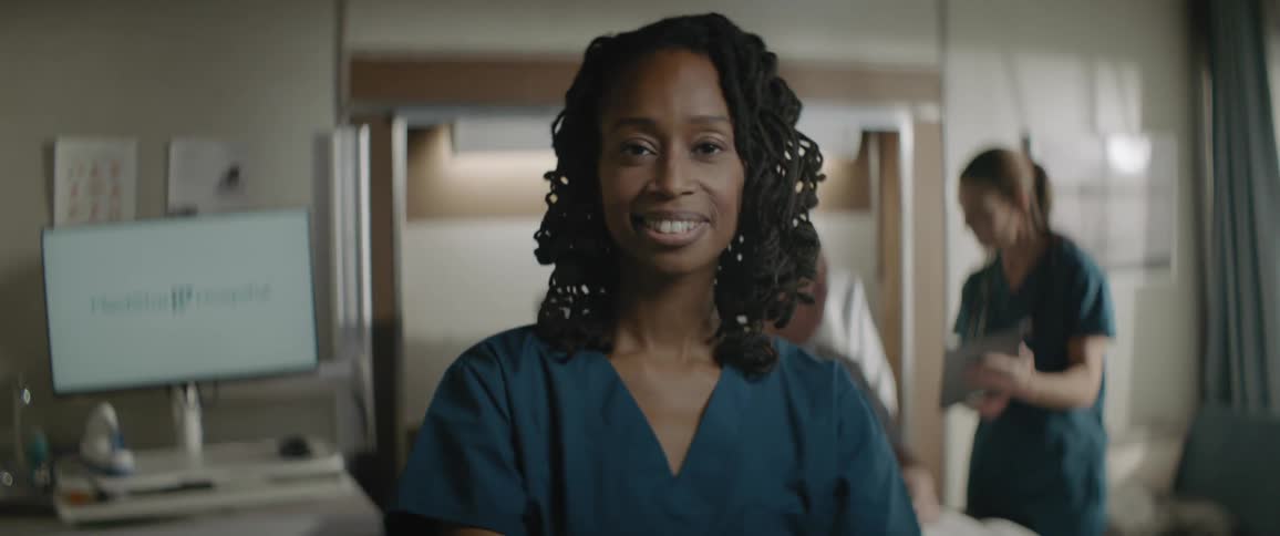 Portrait of one nurse with another nurse attending to a patient in the background