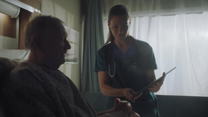 Man gestures to clinician holding tablet indoors near window
