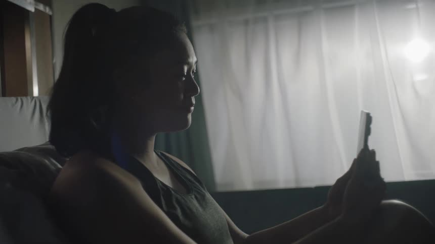Woman with a ponytail and black undershirt makes a video call on a smartphone in a room