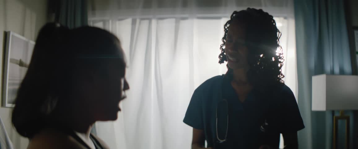 Nurse holding a tablet and talking to a woman who is sitting on the bed in a room