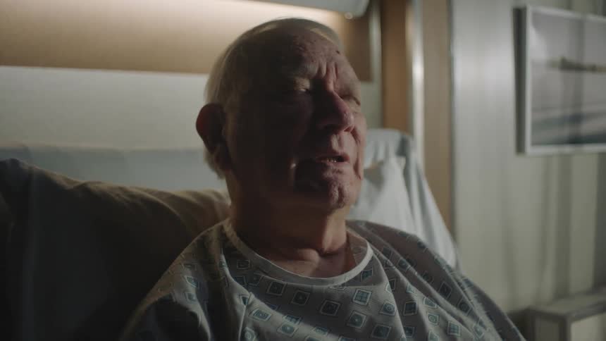 An elderly man sitting on an hospital bed looking sad