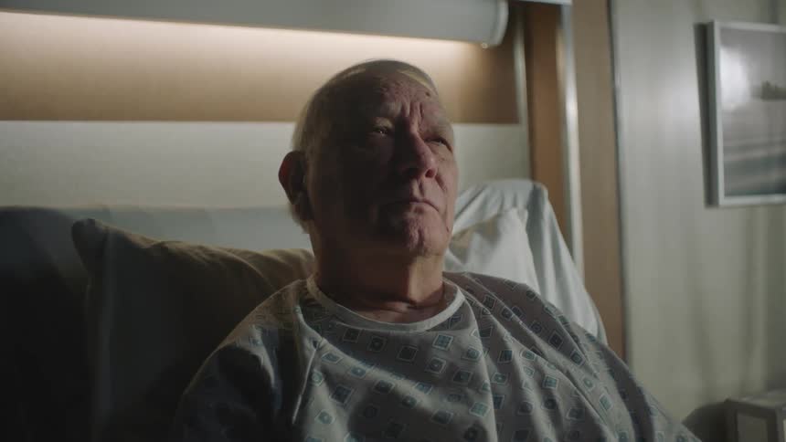 Elderly man looks contemplative sitting in hospital bed