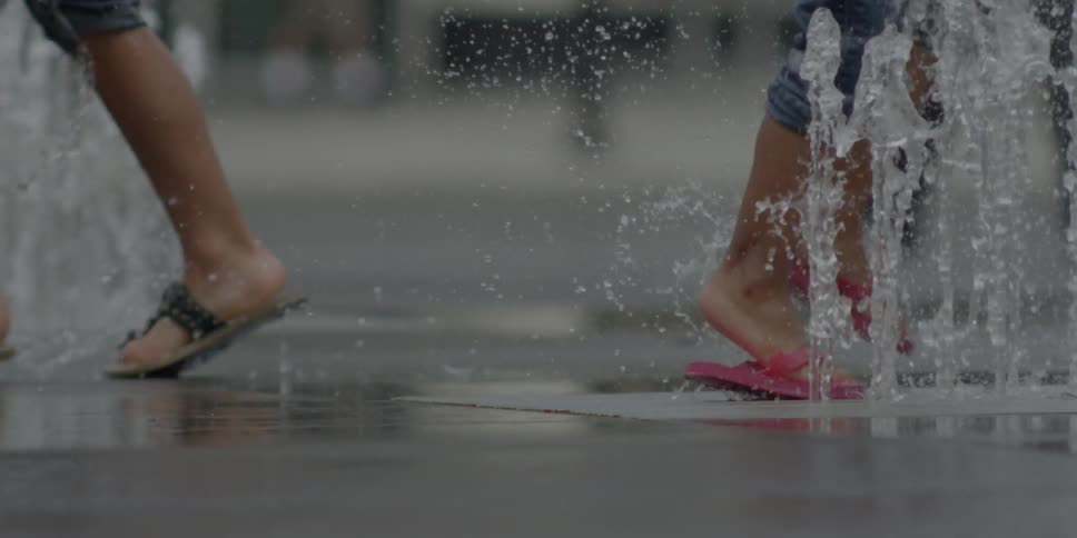Children run through fountains in a concrete-covered area