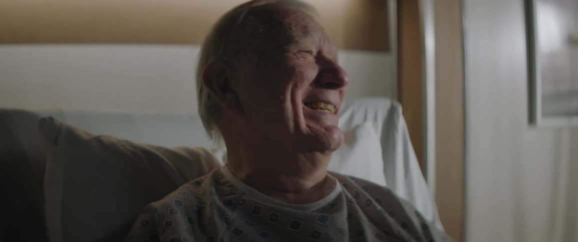 An old man talking and laughing while sitting up in a hospital bed