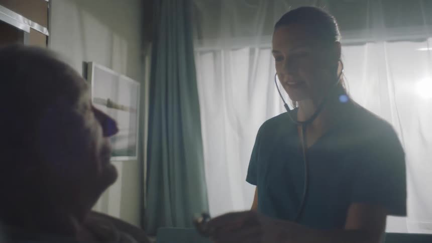 A female doctor talks to an elderly man while listening to his heartbeat with a stethoscope