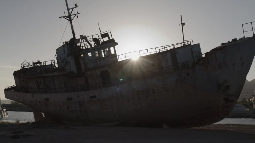 Rusty and weathered ship by the sea with the suns reflection on the horizon
