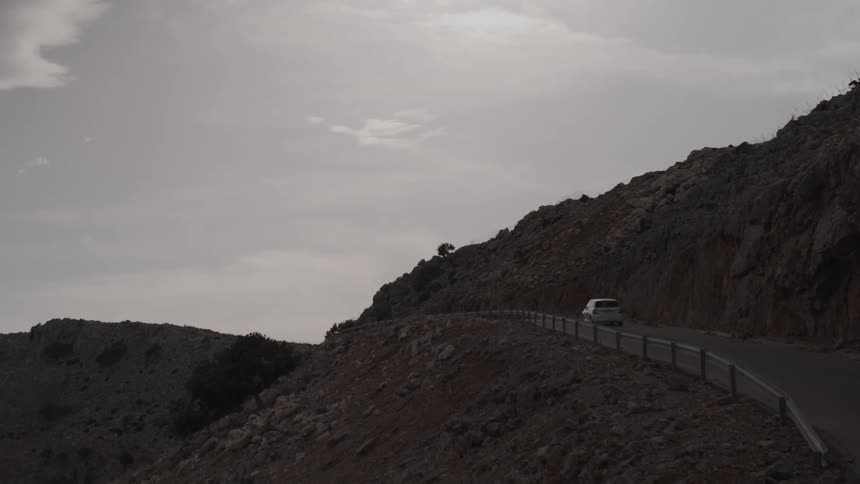 A car driving along a deserted road between rocky hills