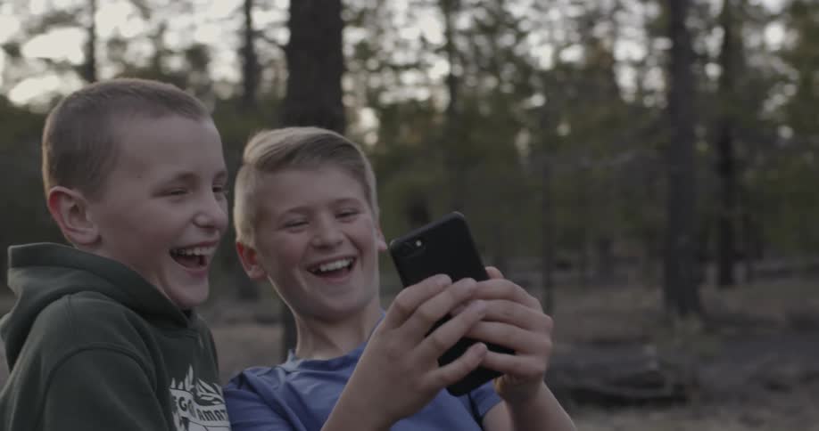 Two boys take selfies and laugh in a wooded area