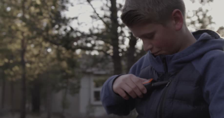 A boy holds a walkie talkie to his chest outside